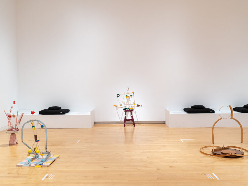 Figurative sculptures sited on a gallery floor with a bench in the background.