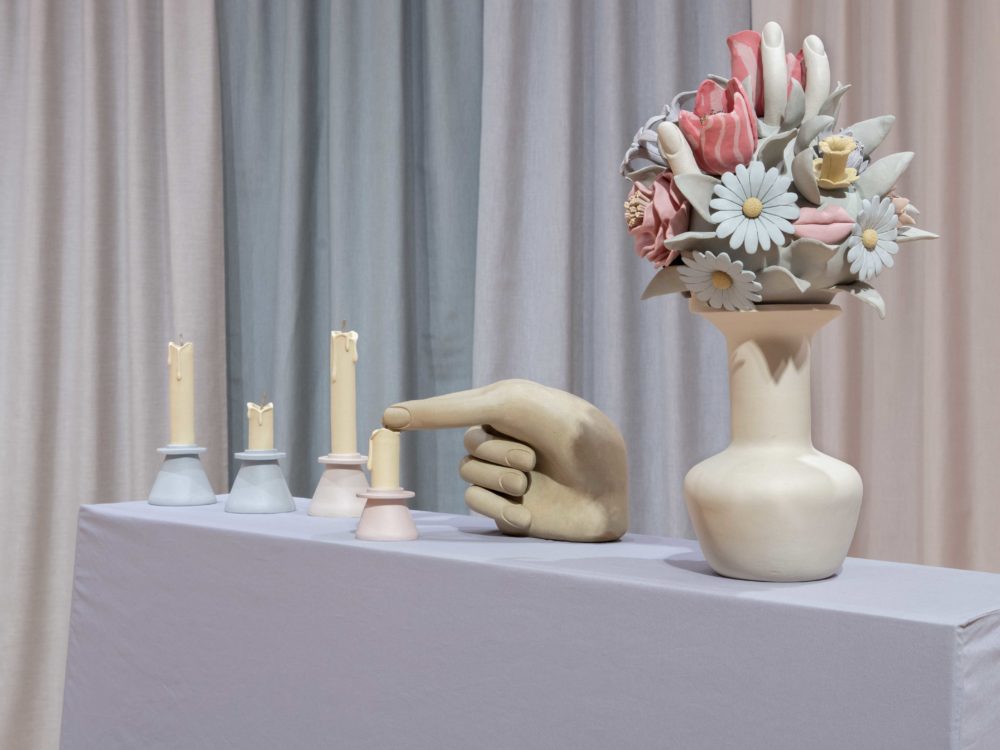 Clay sculptures of extinguished candles with a surrealist bouquet with pastel-colored curtains in the background.