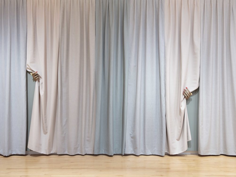 Pastel multi-colored curtain panels with two manicured hands pulling back two pieces of fabric.