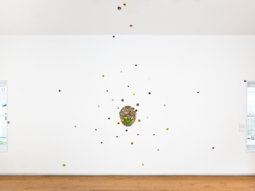 Wall mounted work with small glass flowers hung on the wall surrounding it.