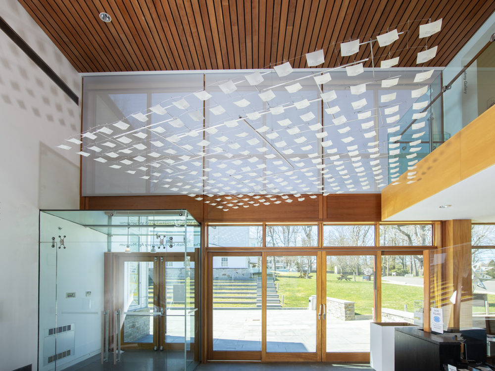 The Museum's atrium with a large suspended sculpture hanging from the ceiling comprised of many white squares o material strung together by wire.