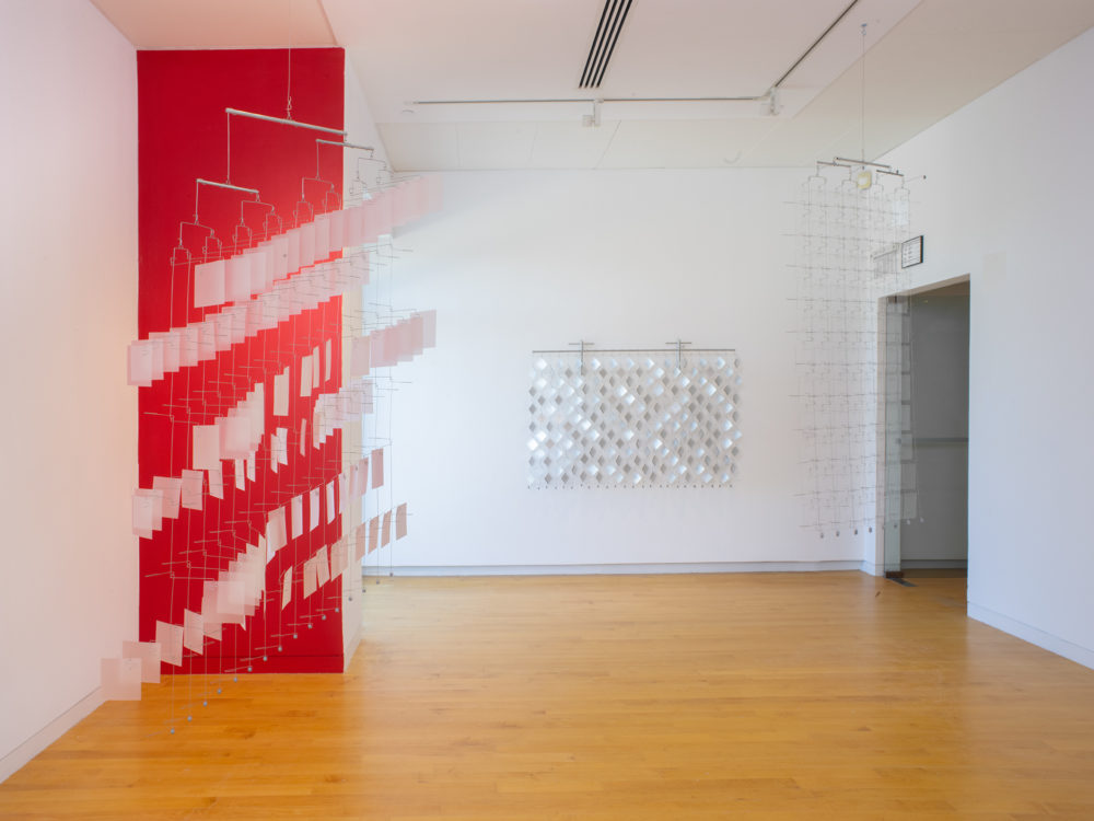 Gallery with one wall painted red and three suspended reflective material and wire sculptures.