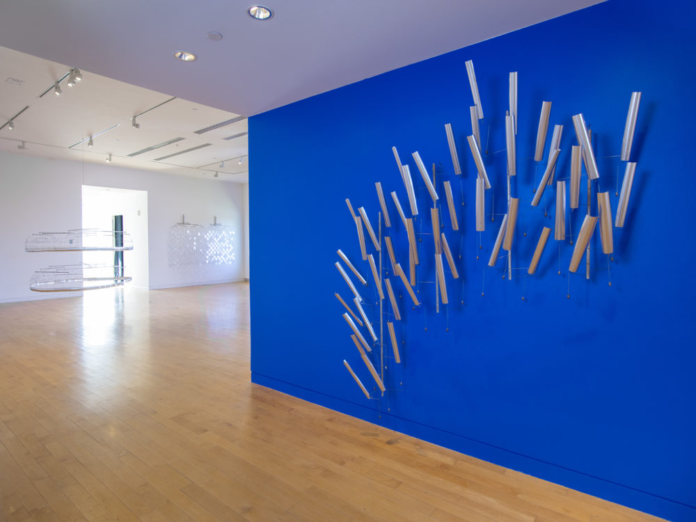 Blue wall in foreground with a silver material and wire sculpture. Two other suspended sculptures in background.