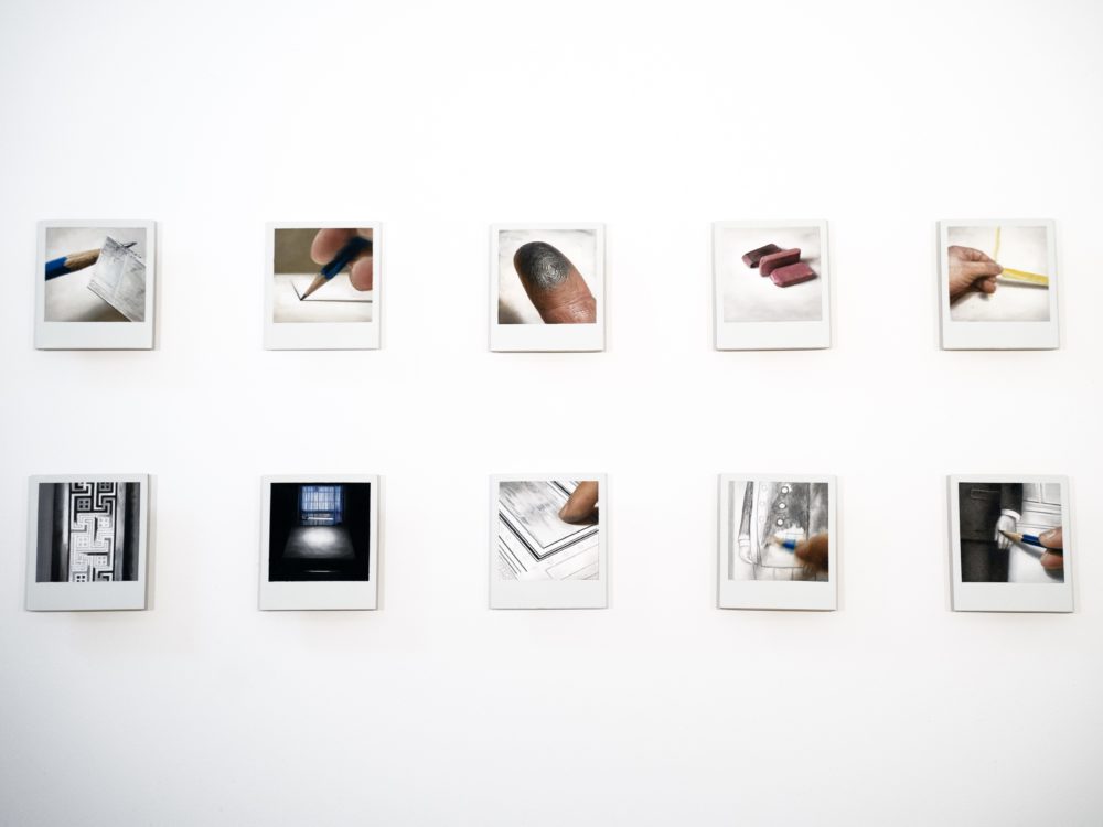 Grid of paintings on Polaroid photographs showing elements of the drawing process, for example pencils, erasers, fingers.