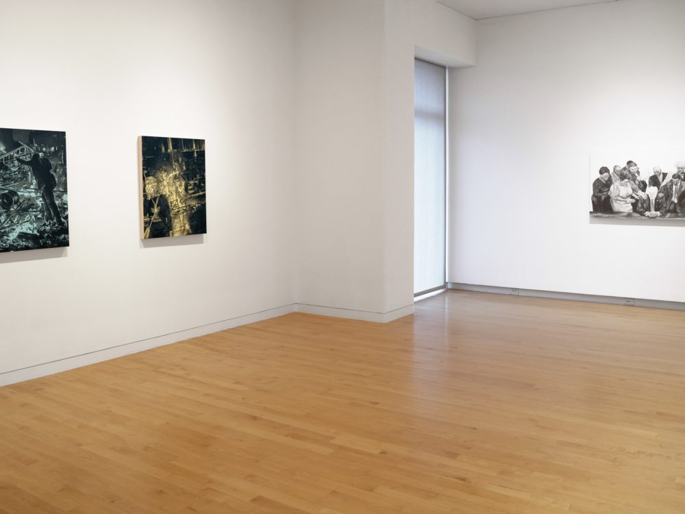 Installation view of gallery with two paintings of protest scenes with black images on single colored backgrounds at left and a black and white drawing at right