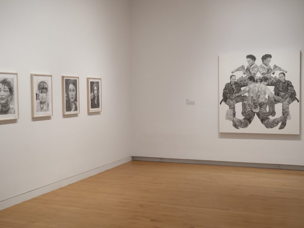 Installation image of gallery with four small black and white drawings on the left wall and one large black and white drawing to the right.