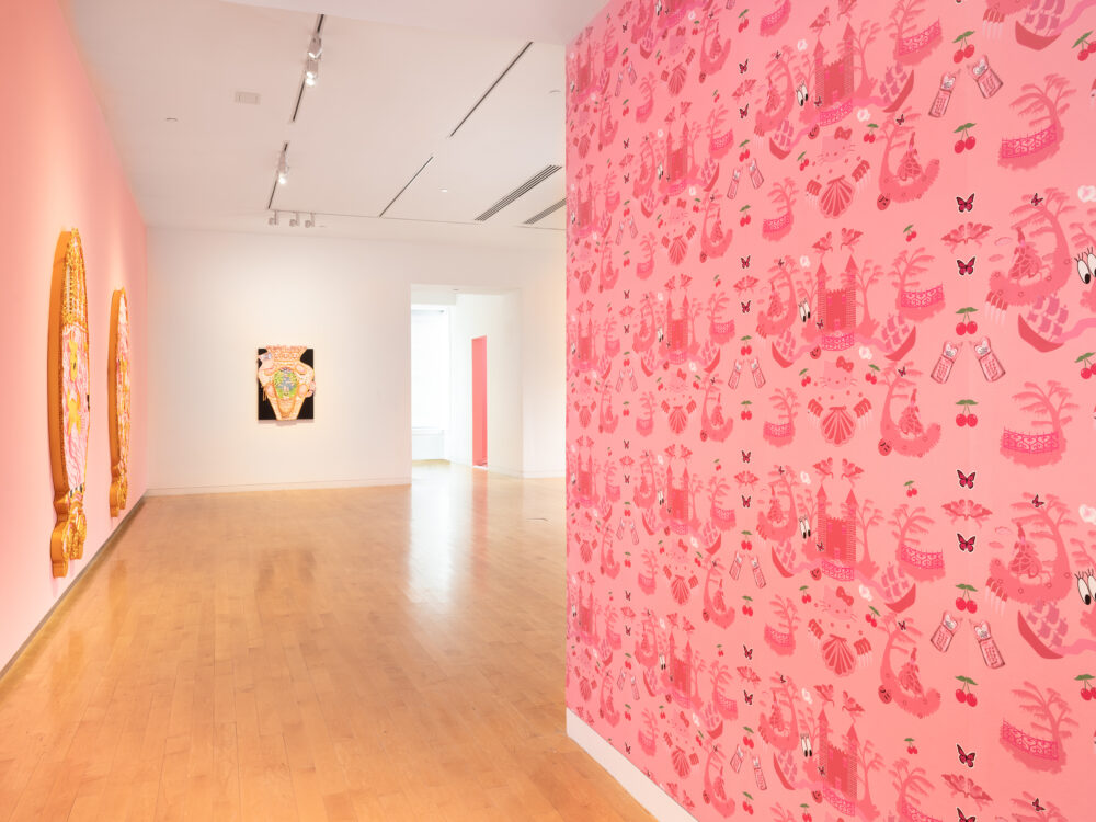 A close up of Yvette Mayorga's artist designed wallpaper to the right and paintings hung on walls to the left.