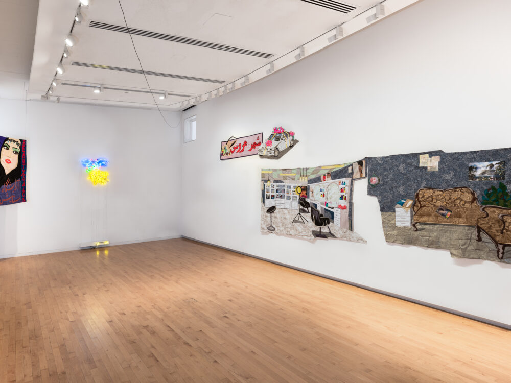 A museum gallery with large-scale tapestries hanging on the walls. A neon sign of a woman's hands with red nails and grapes hangs on the furthest wall.