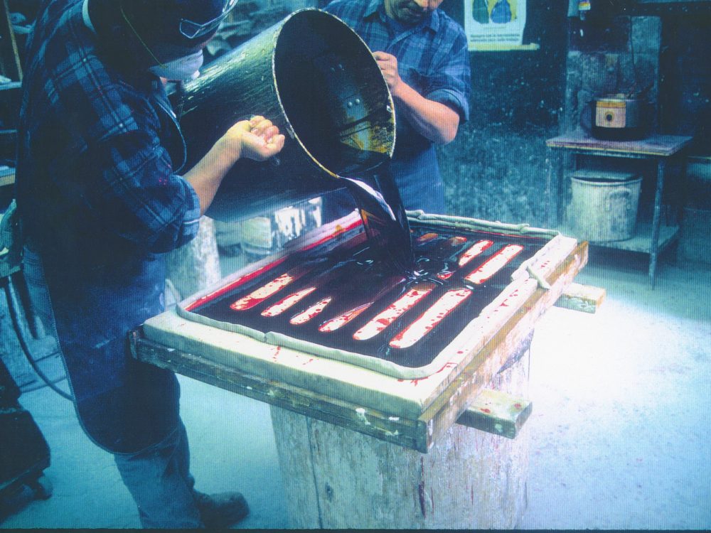 Two men pouring a substance into a mold which looks like a sewer drain