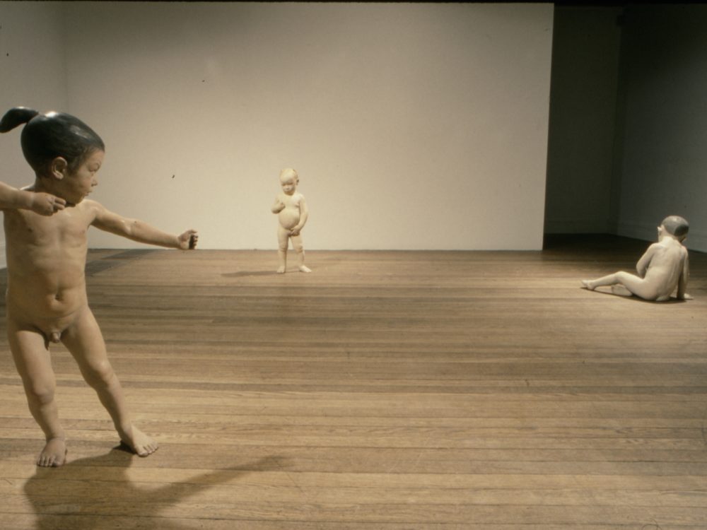 This is an installation done by Judy Fox which features three works that are representations of traditional figures as children in the nude in various poses